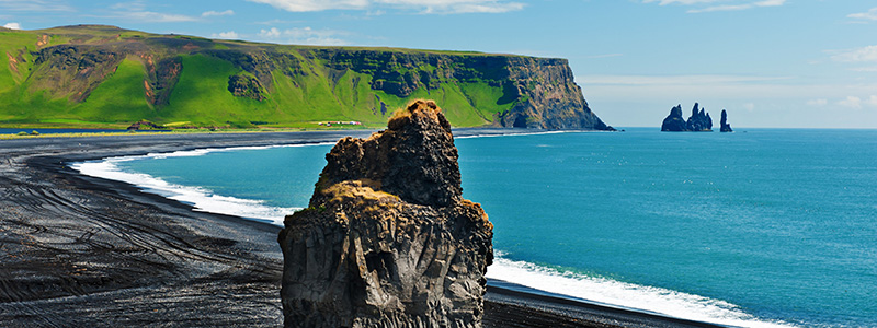 Den svarta stranden med gröna, karga berg på Island.