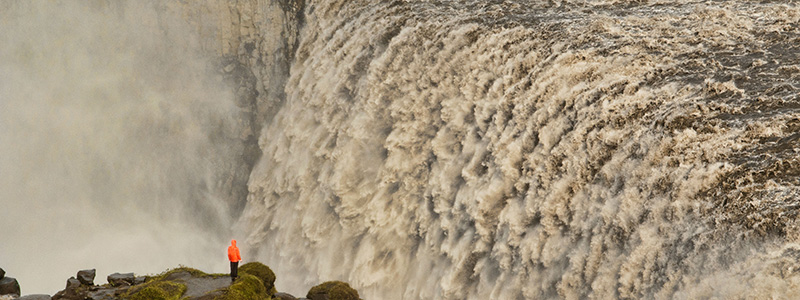 Turist blicker ut över det enorma vattenfallet Dettifoss på Island.