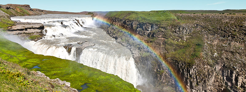 En regnbge ver Gullfoss bland den vilda naturen p Island.