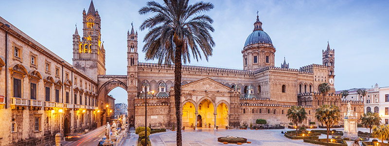 Siciliens huvudstad Palermo med palmer och byggnader i solnedgången.