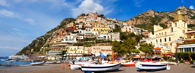Strandnära byn Positano med båtar och hus uppför berget längs Amalfikusten.