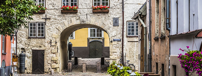 Svenska porten i Riga med kullerstensfasader och blommor.