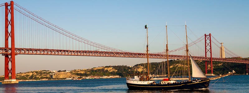 Segelbåt framför den röda hängbron 25 april bron i Lissabon, Portugal.