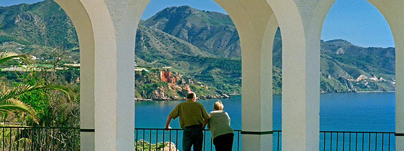 Par som tittar ut över bergen, palmerna och Medelhavet från Balcone de Europe på en solsemester.