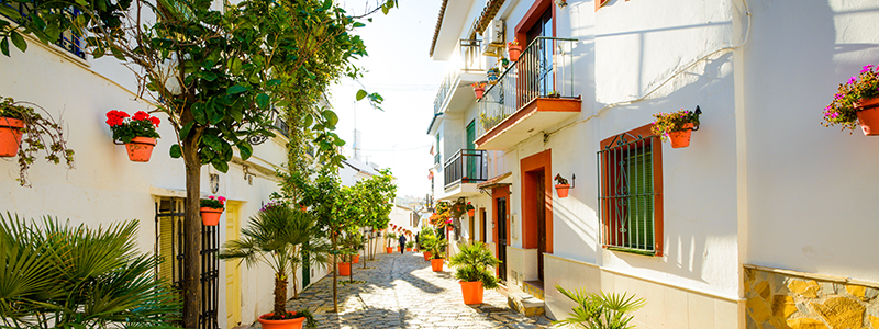 Den andalusiska, vita byn Estepona med vita hus, apelsinträd och konstverk.
