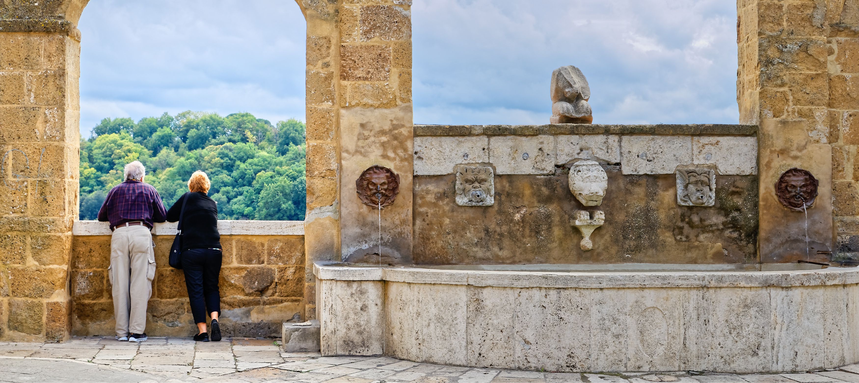 Äldre par njuter av utsikten från en gammal stenbyggnad.