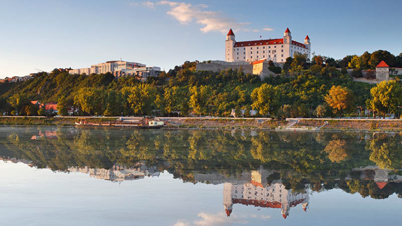 Slottet i Bratislava med den spegelblanka floden och grön natur i omgivningarna.