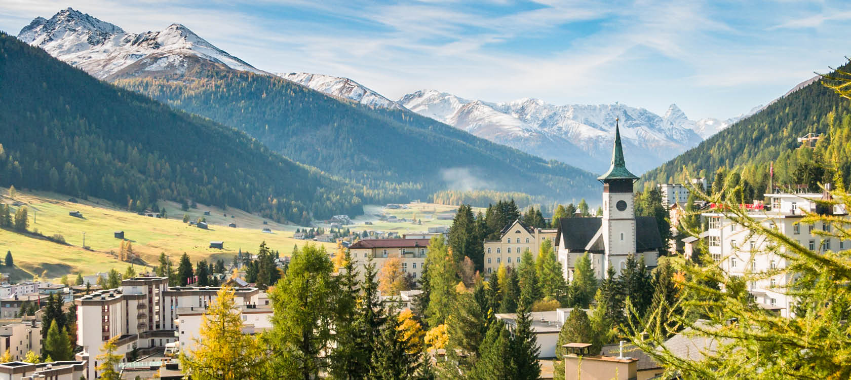 Fjllbyn Davos med grantoppar, berg och torn i Schweiz.